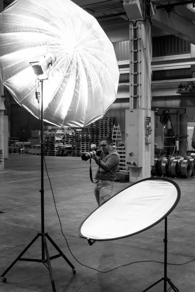 Fashionshooting, Fotograf schaut auf Kamera, im Vordergrund ein großer Lichtschirm, industrieller Hintergrund, Schwarz-Weiß