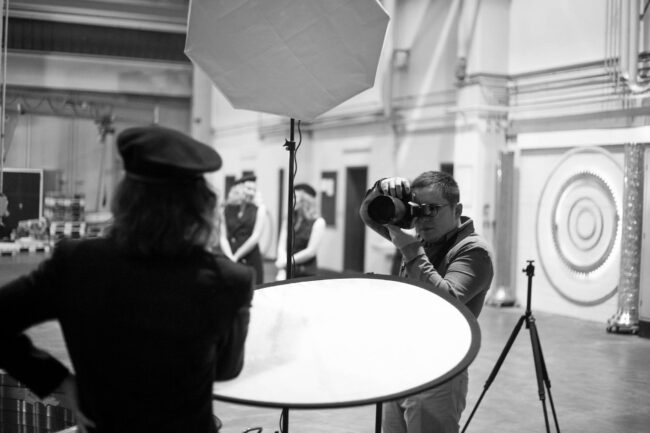 Fashionshooting, Fotograf fotografiert Model in -Uniform, im Hintergrund weitere Models zu erkennen, Making-of Bild, Schwarz-Weiß