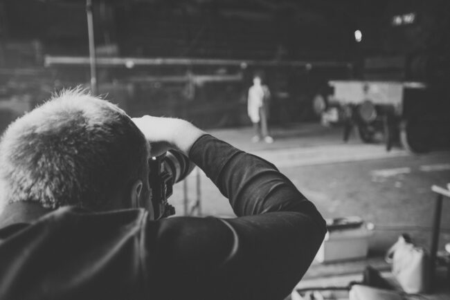 Fashionshooting, Fotograf steht mit dem Rücken zur Kamera und fotografiert ein Model vor industriellem Hintergrund, Schwarz-Weiß