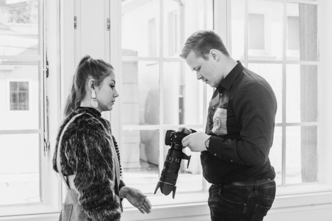 Fashionshooting, Fotograf zeigt Model ein Foto auf dem Kameradisplay, Schwarz-Weiß, Querformat