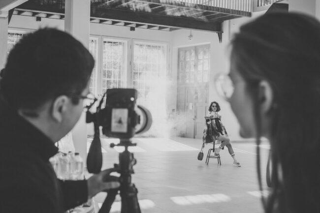 Fashionshooting, Fotograf steht mit Rücken zur Kamera und fotografiert Model, eine Frau schaut auf das Display der Kamera und schaut sich ein Bild an, Schwarz-Weiß