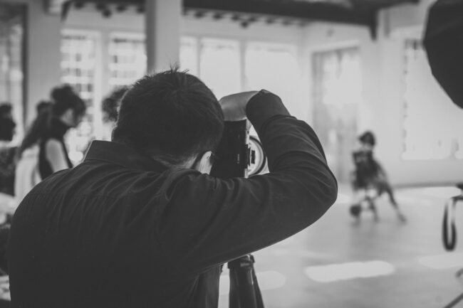 Fashionshooting, Fotograf steht mit Rücken zur Kamera und fotografiert Model, welches unscharf im Hintergrund erkennbar ist, Schwarz-Weiß