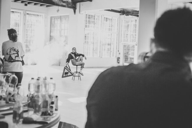 Fashionshooting, Fotograf steht mit Rücken zur Kamera und fotografiert Model, es sind weitere Personen im Bild zu sehen, Schwarz-Weiß