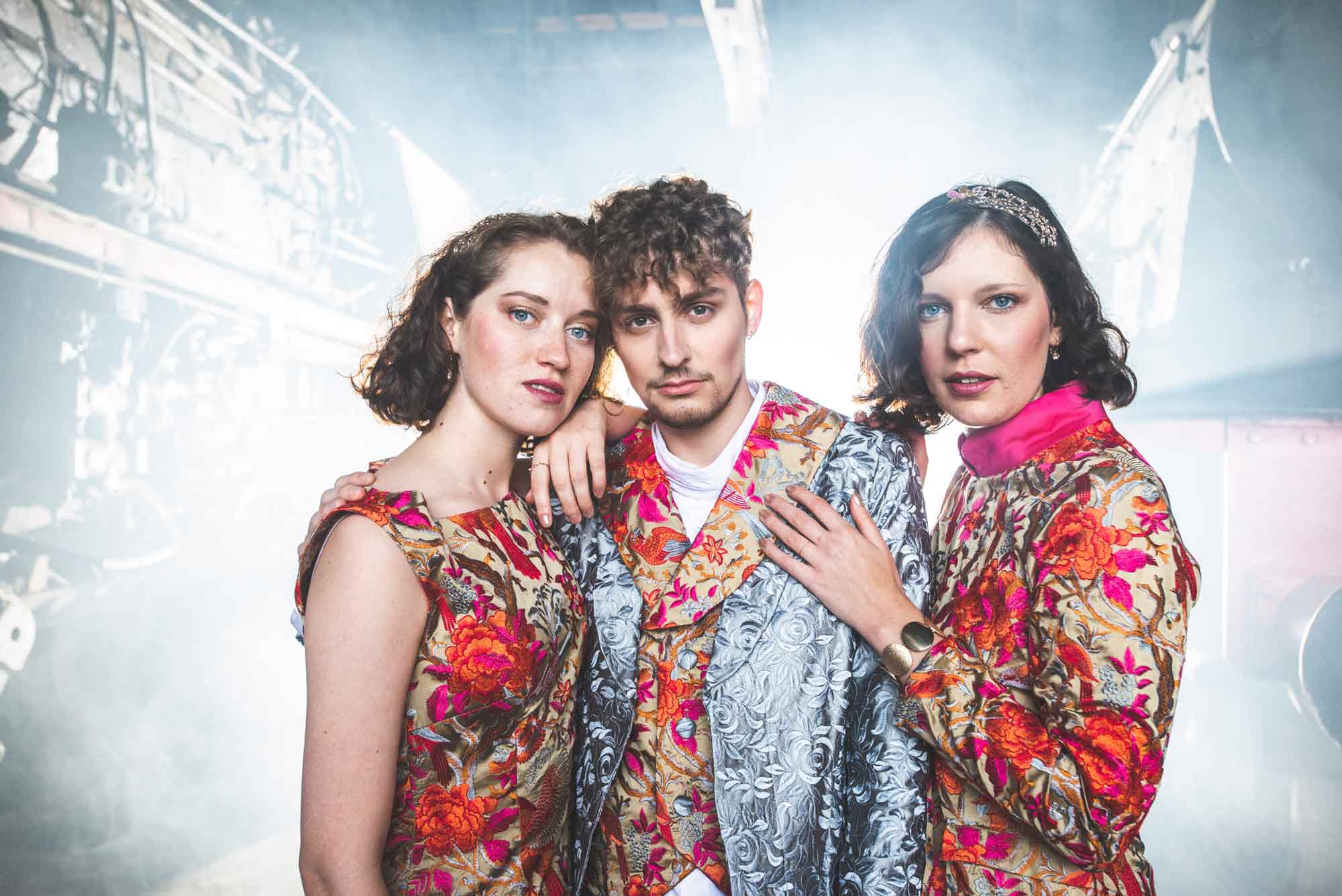 Fashion, 3 Models in bestickten Oberteilen vor industriellem Hintergrund, Beleuchtung von hinten, Querformat