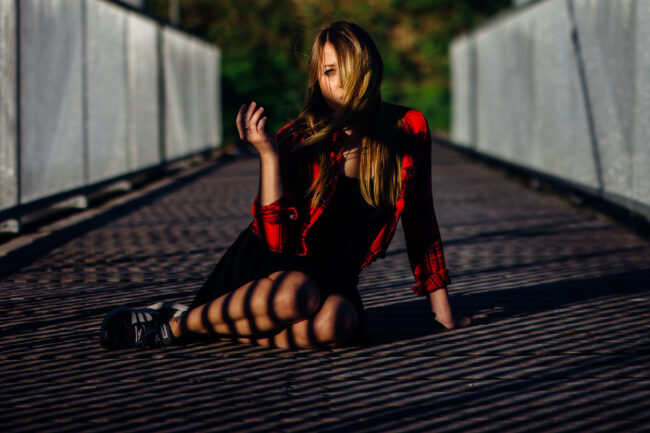portrait, Frau mit roter Bluse sitzt auf Brücke, starkes Licht-Schatten-Spiel durch das Brückengeländer