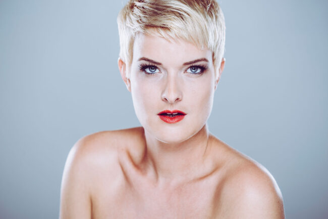Portrait, Frau mit blonden kurzen Haaren und rotem Lippenstift vor neutralem Hintergrund, Nahaufnahme