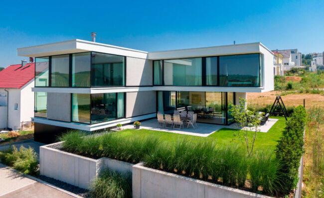 Architektur, modernes quaderförmiges Haus mit 2 Stockwerken und Flachdach, große Fensterfronten, erhöhter Garten mit Terrasse