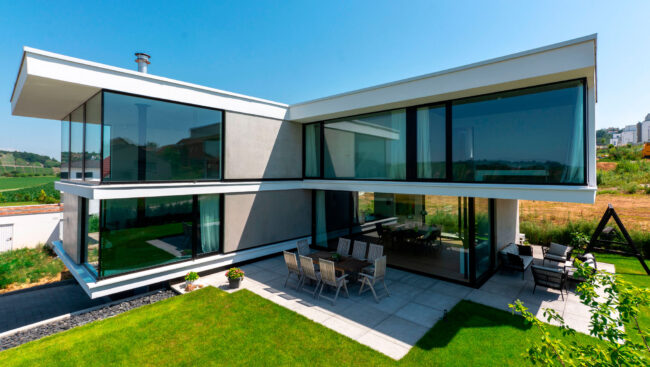 Architektur, modernes Haus über Eck mit großen Fensterfronten und Terrasse vor grünem Garten