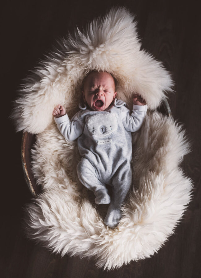 Newborn, gähnendes Baby liegt auf Fell in einer Wanne, Ganzkörperaufnahme von oben