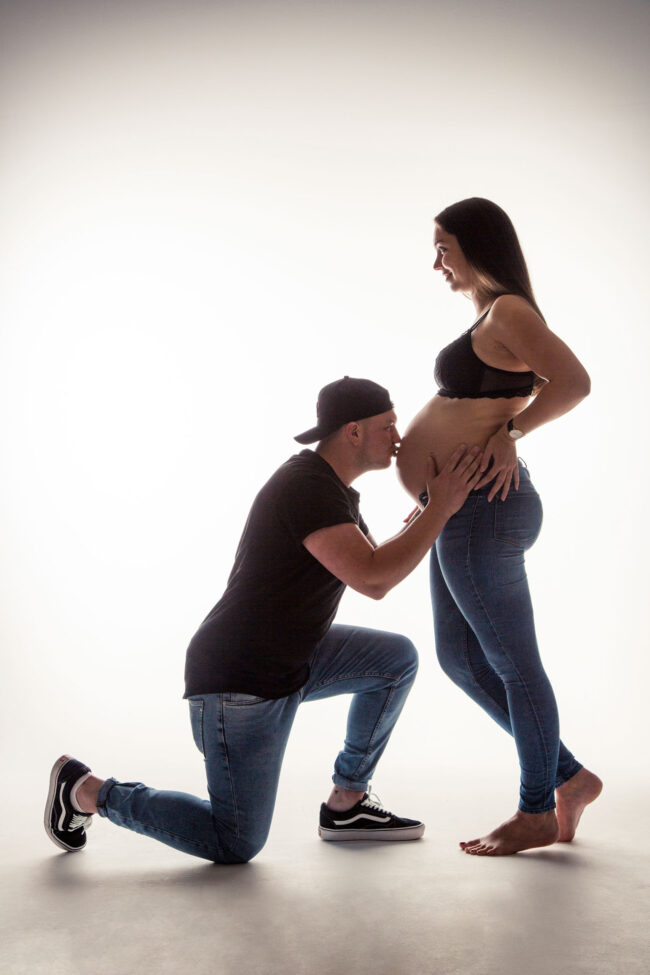 Babybauch, Mann auf einem Knie küsst den Babybauch der Frau, Ganzaufnahme, Studioaufnahme