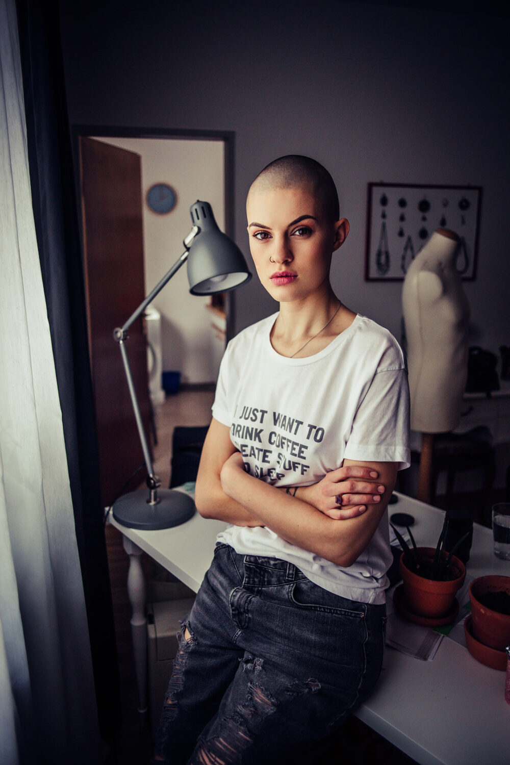 Portrait, junge Frau mit abrasierten Haaren an Tisch gelehnt mit Fensterlicht