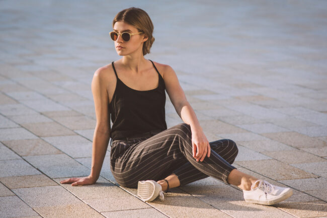 Portrait, Junge Frau mit Sonnenbrille im Schneidersitz auf Betonpflaster