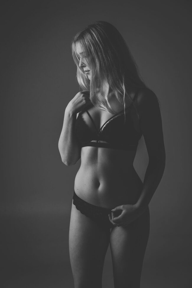 Sensual, Frau in schwarzer Wäsche schaut nach links unten, eine Hand am Schlüsselbein, Schwarz-Weiß