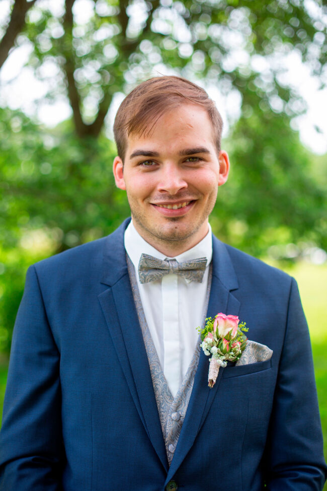 Hochzeit, Portrait, Halbaufnahme von Brautigam in blauem Sack im Grünen