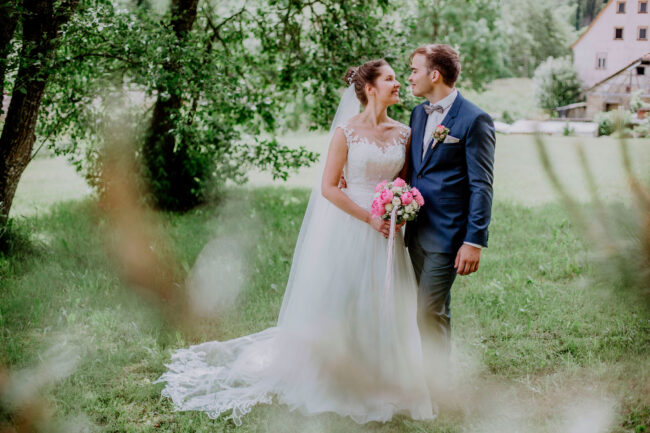 Hochzeit, Portrait, Outdoor, Brautpaar steht auf Wiese unter einem Baum und schaut sich an, Querformat