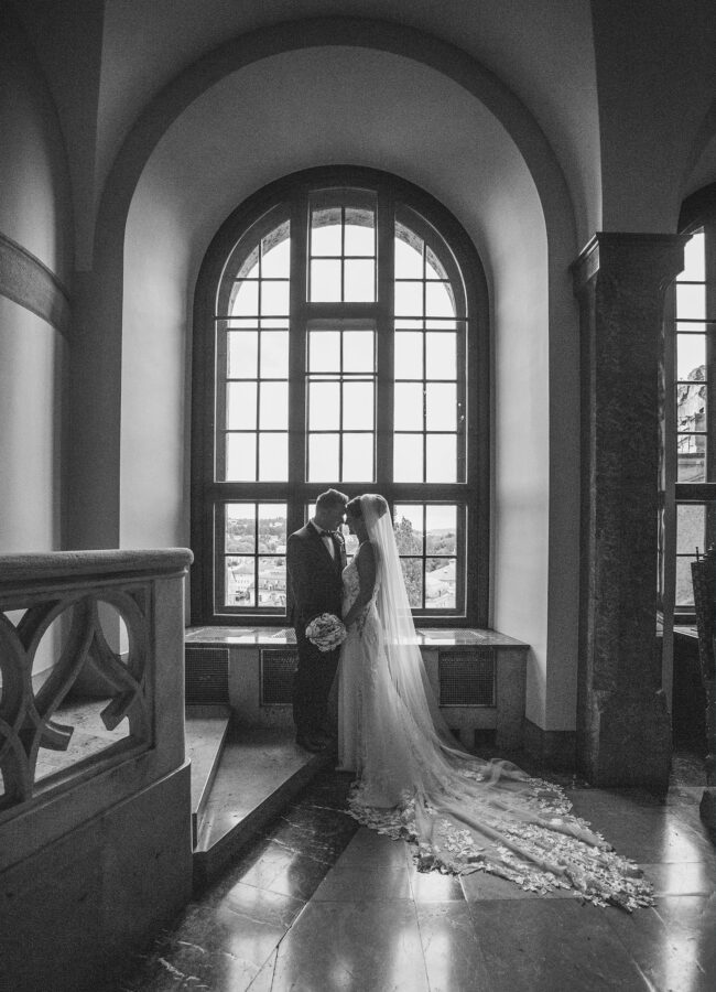 Hochzeit, Brautpaar steht vor Bogenfenster und lehnt die Stirn gegeneinander, Ganzbild, Hochformat, schwarz-weiß