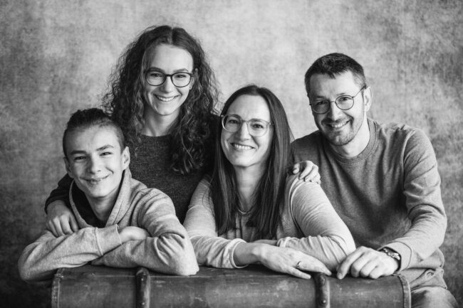 Familien, Eltern mit zwei Teenagern lehnen auf Koffer, alle strahlen in die Kamera, Schwarz-Weiß