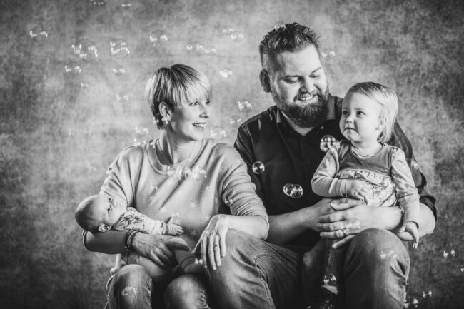 Familie, Eltern mit Kleinkind und Neugeborenem auf den Armen, mit Seifenblasen, Schwarz-Weiß