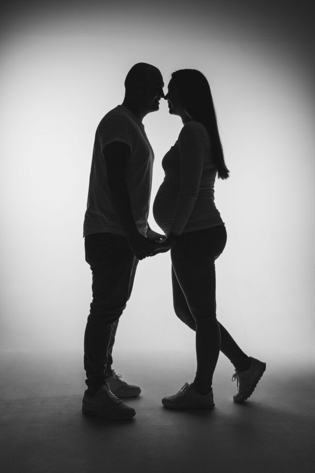 Babybauch, Mann und schwangere Frau stehen sich gegenüber und halten sich an den Händen, Schwarz-Weiß