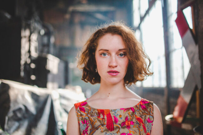 Fashion, Model in besticktem Oberteil schaut in die Kamera, Nahaufnahme, vor industriellem Hintergrund, Querformat