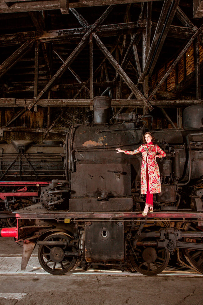 Fashion, Model in besticktem Oberteil steht auf einer alten Lokomotive, industrieller Hintergrund, Hochformat