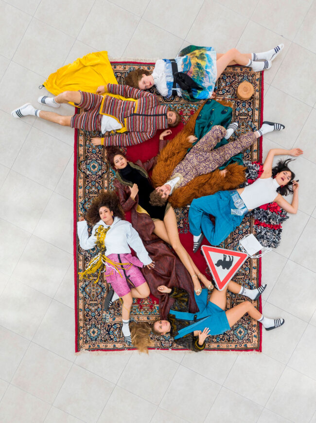 Fashion, Gruppe an Models in bunten Outfits liegt auf einem Teppich, Aufnahme von oben