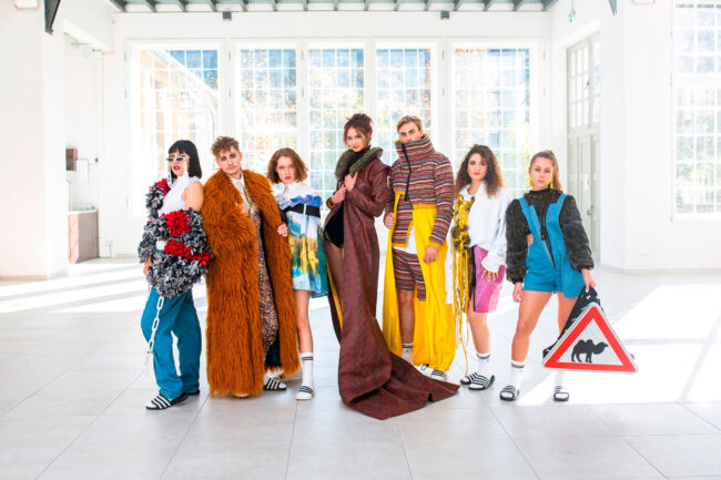 Fashiongruppe, Models in verschiedenen Outfits in heller Halle stehend, hohe Fenster im Hintergrund, Ganzaufnahme, Querformat