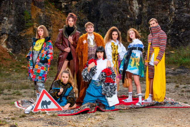 Fashion, Models in verschiedenen bunten Outfits stehen auf Teppich vor Felswand, Querformat, Ganzaufnahme