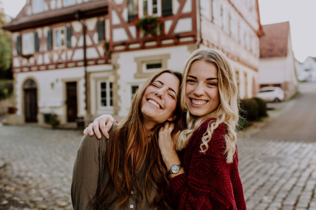 Freundschaftsshooting, zwei Frauen vor Fachwerkhaus strahlen in die Kamera, Nahaufnahme