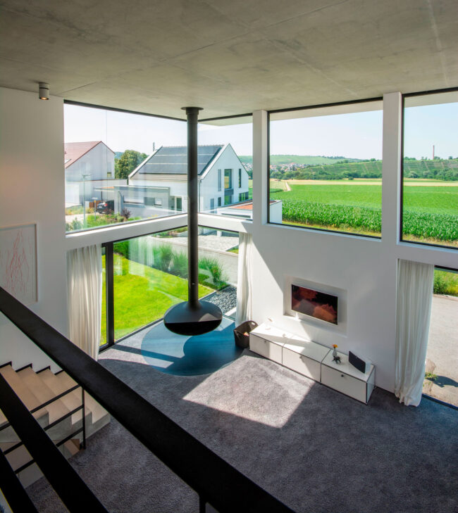 Architektur, Innenaufnahme, Wohnzimmer mit dunklem Teppichboden und großer Fensterfront, seitlich ist ein Treppenaufgang