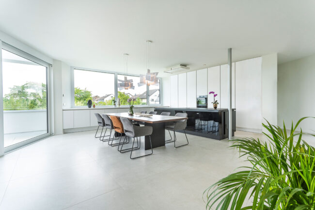 Architektur, Interieuraufnahme geräumige Küche mit Essbereich, bodentiefe Fenster, graue Fliesen und weiße Küche mit modernem Holztisch und grauen Stühlen