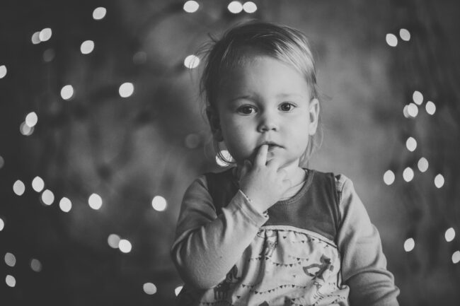 Familie, Kleinkind schaut in die Kamera, hat Zeigefinger an den Mund gelegt, Nahaufnahme, Schwarz-Weiß