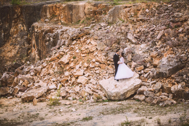 Hochzeit, Outdoor, Brautpaar steht auf Felsbrocken und schaut sich an. Im Hintergrund ist eine Felswand mit Steinbruch