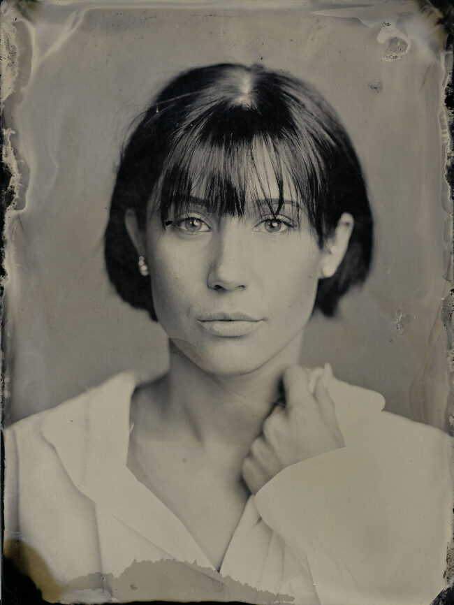 Nassplatte, Schwarz-Weiß, Portraitaufnahme von junger Frau mit dunklen kurzen Haaren und weißer Bluse, Hand greift an den Kragen der Bluse