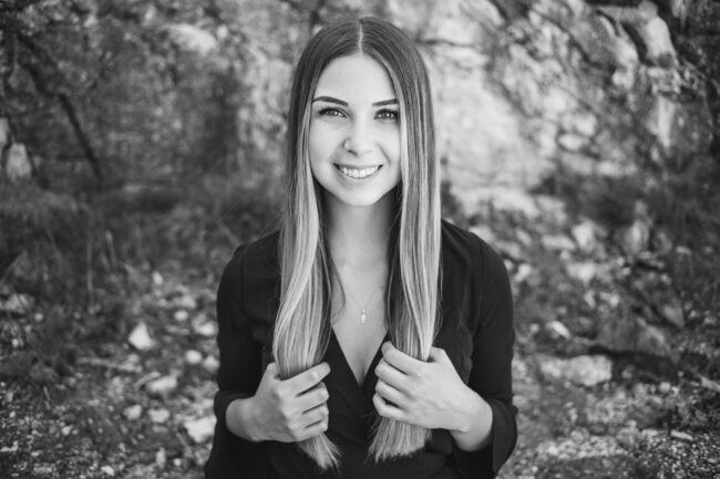 Portrait, junge Frau in dunkler Bluse mit Händen an den Haarspitzen, Nahaufnahme, Schwarz-Weiß