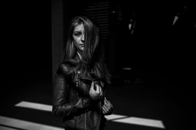 Portrait, Frau mit Lederjacke und Haaren halb vor Gesicht, vor dunklem Hintergrund, Schwarz-Weiß, Halbportrait