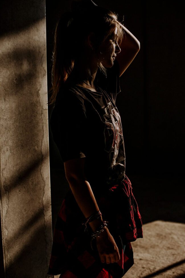 Portrait, Frau im Profil, hält die Haare zu einem Zopf zusammen, trägt ein dunkles Shirt mit rotem Hemd um die Hüfte gebunden, schwarzer Hintergrund, Halbaufnahme