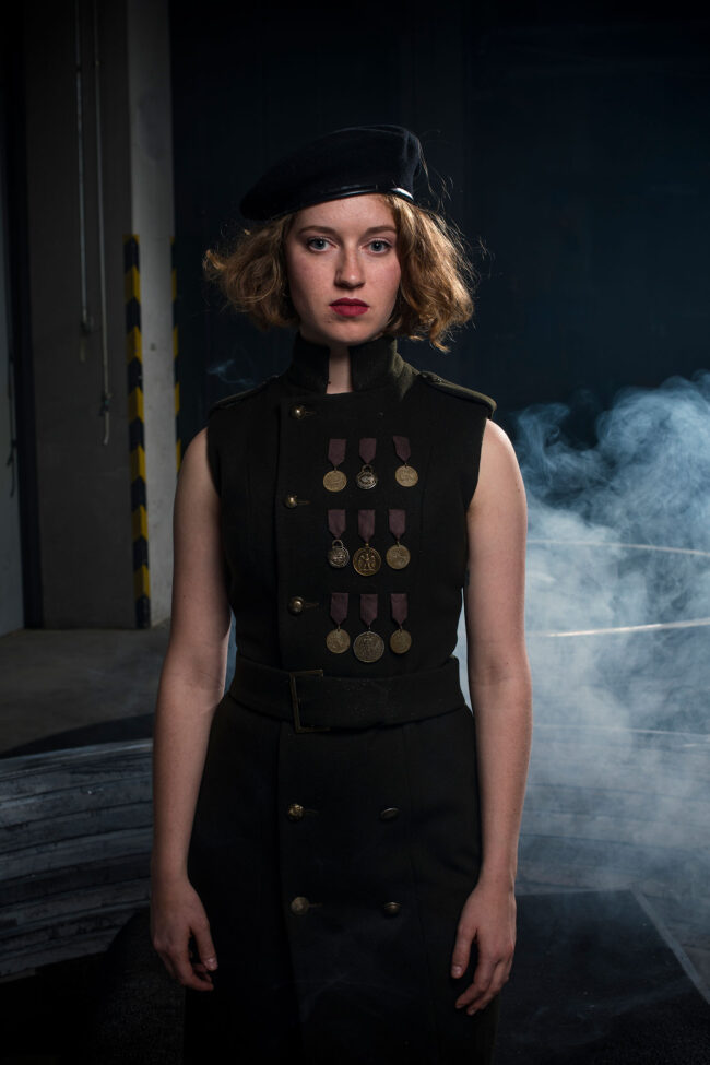 Fashion, Model in einem ärmellosen knielangen dunkelgrünen Kleid, im Stil der 30er Jahre mit breitem Gürtel und 3 Reihen Orden auf der Brust als Verzierung, Halbbild