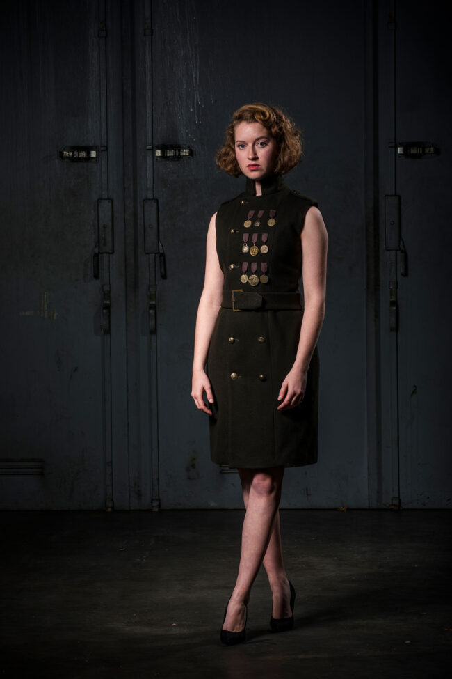 Fashion, Model in einem ärmellosen knielangen dunkelgrünen Kleid, im Stil der 30er Jahre mit breitem Gürtel und 3 Reihen Orden auf der Brust als Verzierung