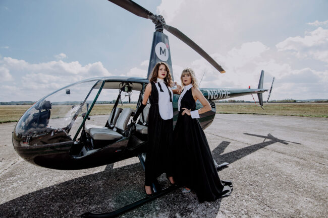 2 Models in schwarz-weißen Kleidern vor einem Hubschrauber, Querformat