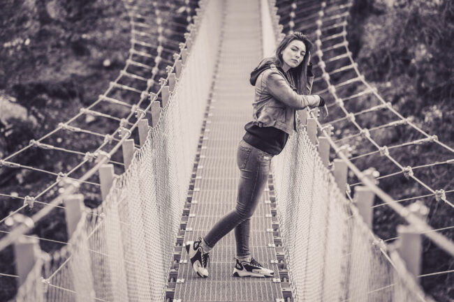 Portrait, junge Frau steht auf Hängebrücke an Geländer gelehnt, Ganzaufnahme, Schwarz Weiß