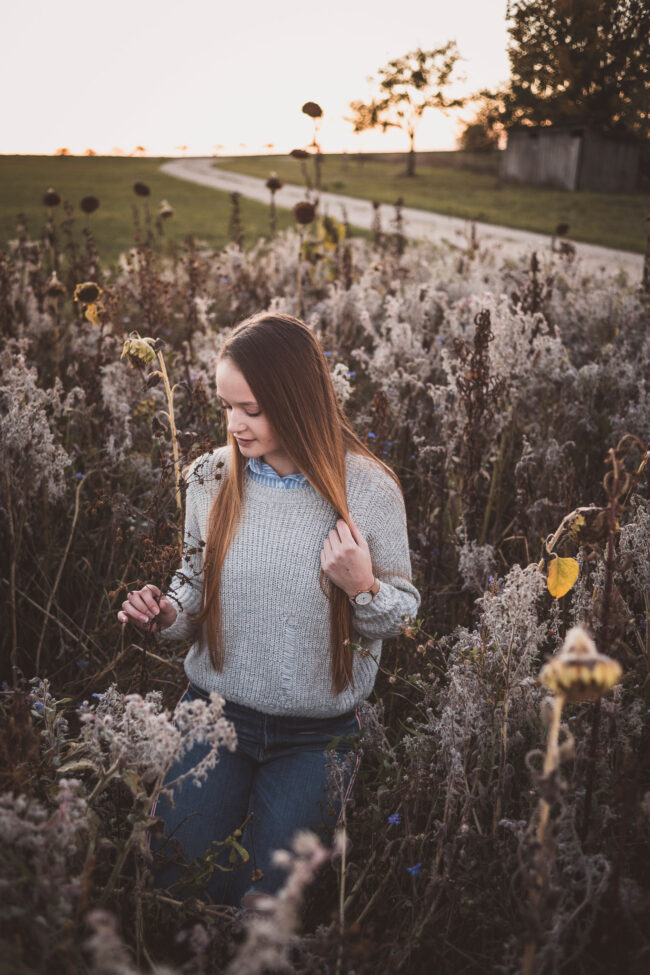 Portrait, junge Frau kniet im herbstlichen Feld mit verwelkten Blumen