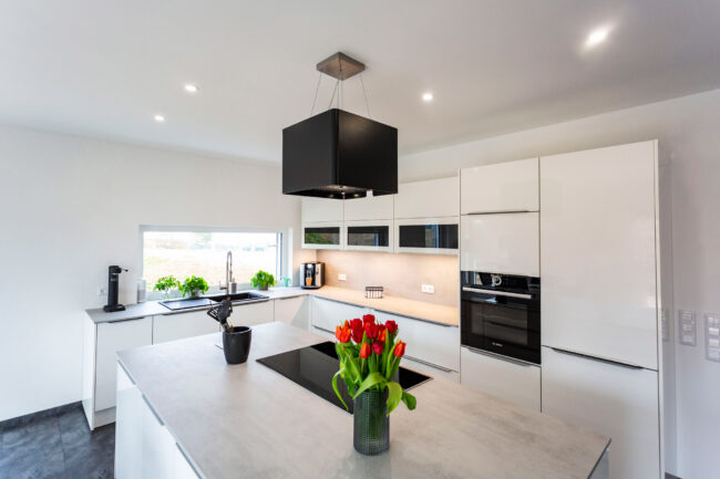 Interieur Küche, freistehende Küchenzeile mit Herd, weißen Schränken, eine Vase mit roten Tulpen steht auf dem Tisch