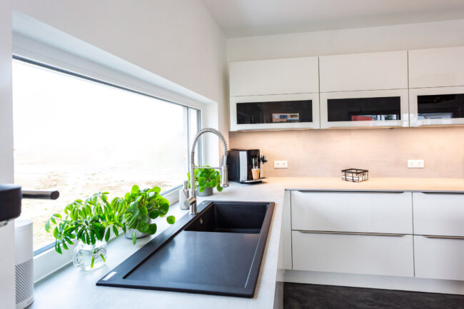 Interieur Küche, helle Küchenzeile mit schwarzem Spülbecken, weiße Wandschränke im Hintergrund
