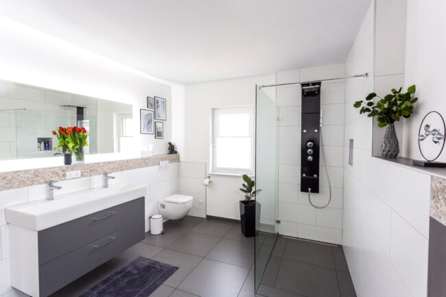 Interieur Badezimmer, schwarze Bodenfliesen, weiße Wände, mit großem weißen Waschbecken und Dusche mit Glaswand