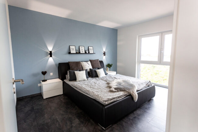 Architektur, Interieur Schlafzimmer, Dunkler Boden, Boxspringbett, bodentiefes Fenster, hellblaue Stirnwand mit schwarzen Wandstahlern