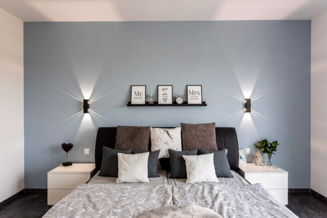 Architektur, Interieur Schlafzimmer, Dunkler Boden, Aufnahme des Bettkopfteil vor einer hellblauen Stirnwand mit schwarzen Wandlampen