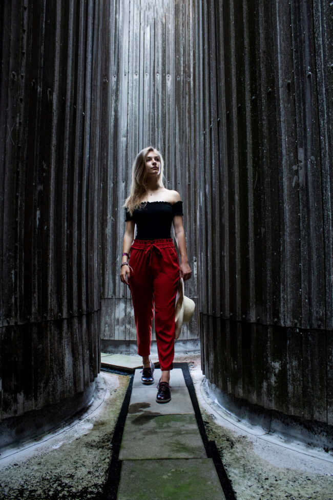 Portrait, Outdoor, junge Frau mit roter Hose geht zwischen zwei Mauern hindurch, Ganzaufnahme