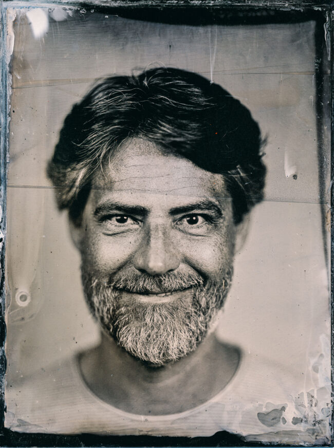 Nassplatte, Schwarz-Weiß, Portraitaufnahme von einem lächelnden Mann mir Vollbart und etwas längeren Haaren