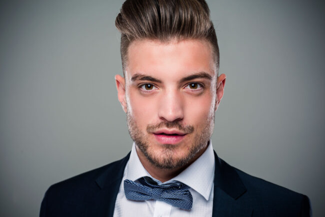 Portrait, junger Mann in Anzug und Fliege schaut neutral in die Kamera